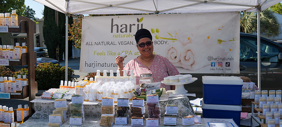 Harji naturals owner smiling in her booth at the 25th Ave Farmers' Market 