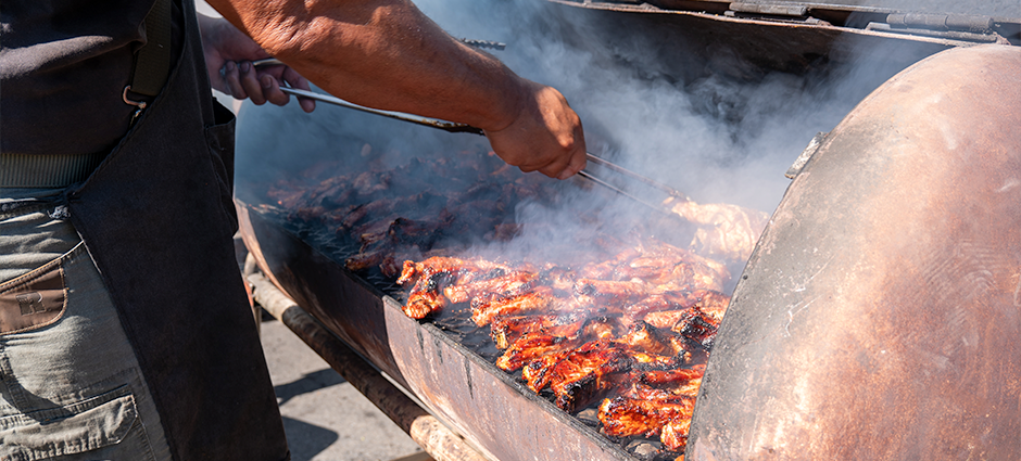 A man's arm works a pair of tongs over a grill full of meats at the Ofa's Island stall at the Dublin Farmers' Market