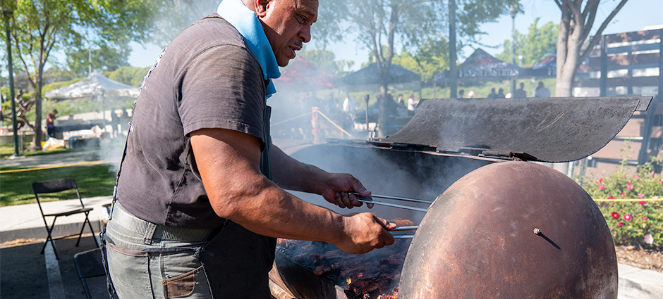 Ofa's Island BBQ owner, a braided man, cooking meats on a large homemade grill at the Dublin Farmers' Market