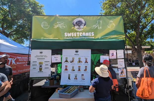 Sweet canes booth at the Irvington Farmers Market. A customer is looking at the pictures on their menu of many smoothie varieties