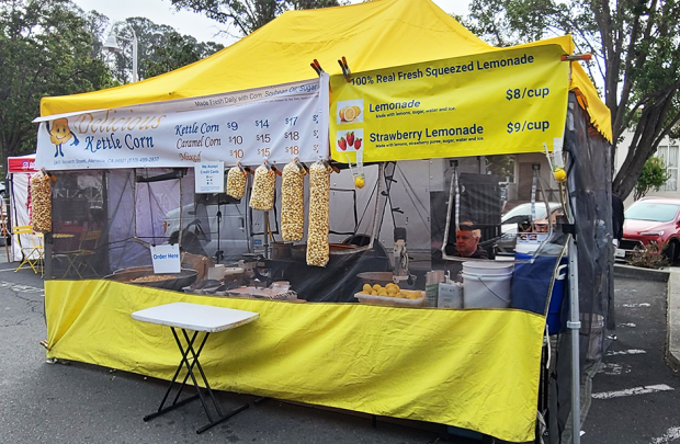 Delicious Kettle Corn tent in the Irvington Farmers' Market with bags of popped corn hanging from the front of the tent