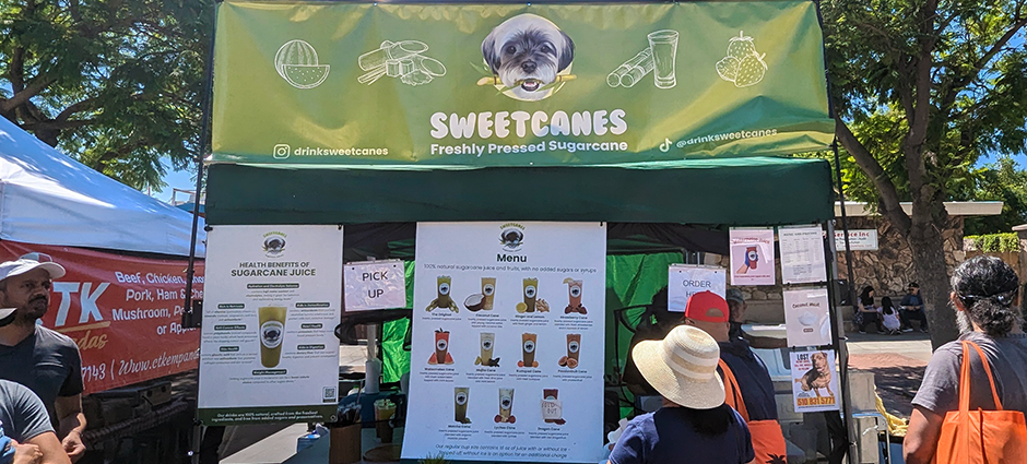 Sweet canes booth at the Irvington Farmers Market. A customer is looking at the pictures on their menu of many smoothie varieties