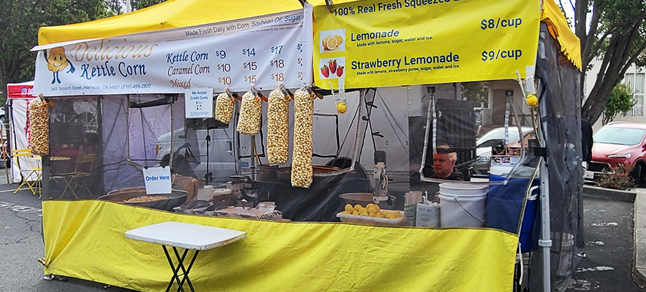 Delicious Kettle Corn tent in the Irvington Farmers' Market with bags of popped corn hanging from the front of the tent