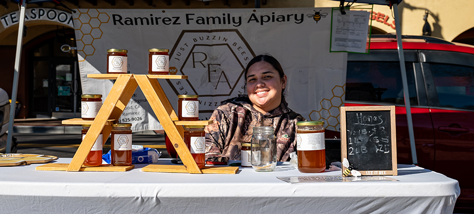 Vendor at the booth behind a rack of honey at the Ramirez Apiary stall